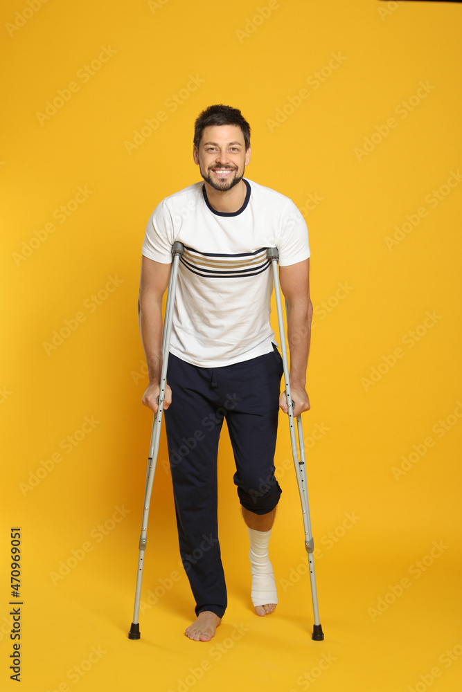 Man with injured leg using crutches on yellow background Man with injured leg using crutches on yellow background