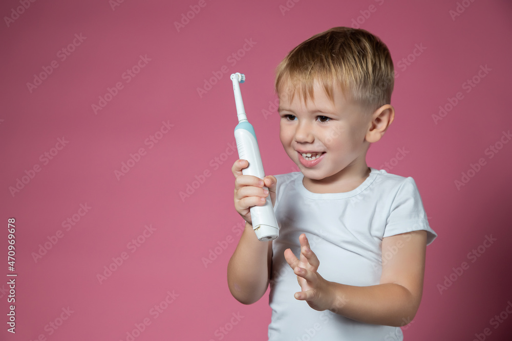 Smiling caucasian little boy holds electric sonic toothbrush on pink background Smiling caucasian little boy holds electric sonic toothbrush on pink background