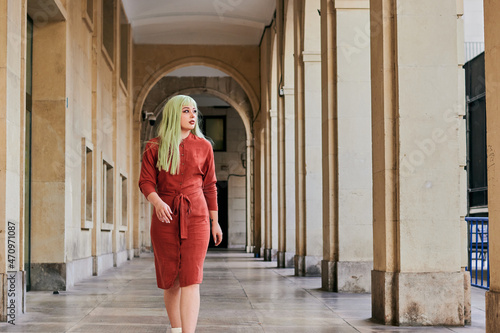Alternative woman with green hair and red dress walks in old building