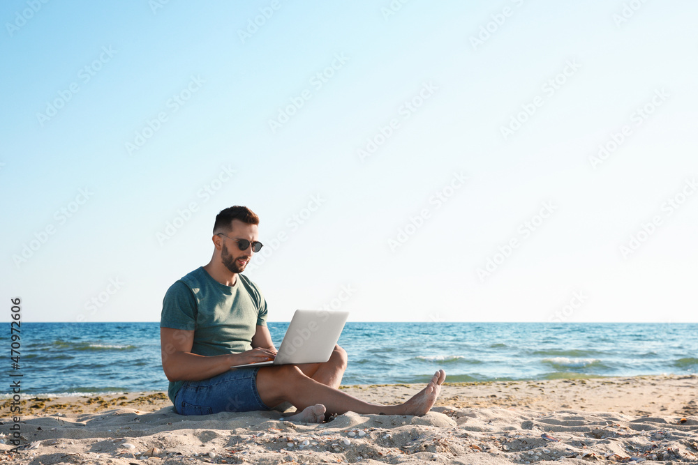 Man working with laptop on beach. Space for text