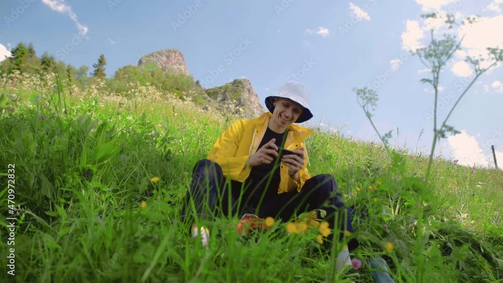 A young man is sitting on a slope and playing a game on his phone in a mountainous area. Tourism and travel A young man is sitting on a slope and playing a game on his phone in a mountainous area. Tourism and travel