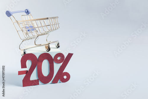 An empty metal basket from the store on a light podium and the figure -20% on a blue background close-up. The concept of discounts and sales in trade