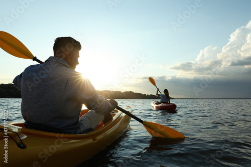 Couple kayaking on river at sunset, back view. Summer activity