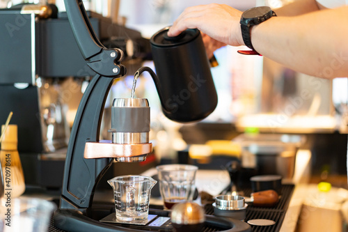 Selective focus of a professional Barista's hand pouring hot water from a kettle into the stainless cup on a coffee dripped stand, making a drip coffee to a measuring glass beaker in a blurred counter