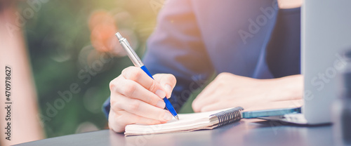 Obraz na płótnie Woman hand writing on a notepad with a pen and she is holding a cell phone in the office. w salonie