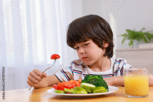 Cute little boy refusing to eat vegetables at home photo