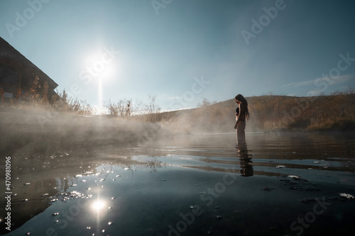 Woman relaxing at hot spring. First frost, hot water, beautiful wooden house in colourful autumn landscape