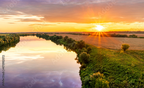 Scenic view at beautiful summer river sunset with reflection on water with green bushes, grass, golden sun rays, calm water ,deep cloudy sky and glow on a background, spring , evening landscape © Yaroslav
