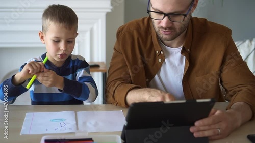 Online education of preschoolers at home. Cute little child chooses yellow marker to draw with parent holding tablet computer help at table closeup spbd photo