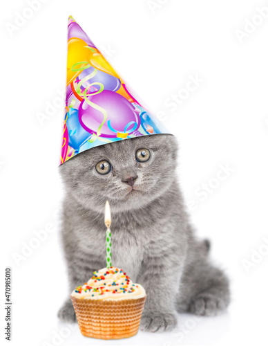 Fototapeta Naklejka Na Ścianę i Meble -  Kitten wearing birthday cap sits cup cake and looks at camera. isolated on white background