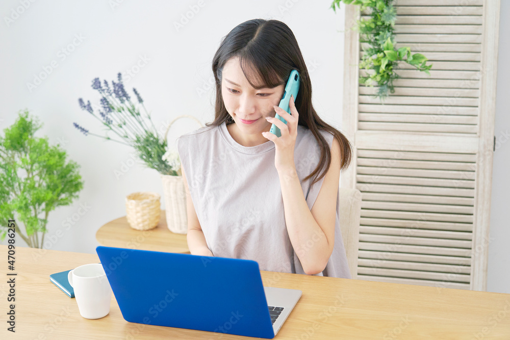 パソコンを見て電話する女性　リビング