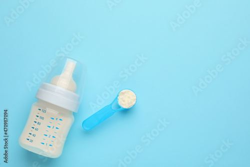 Feeding bottle with infant formula and powder on light blue background, flat lay. Space for text