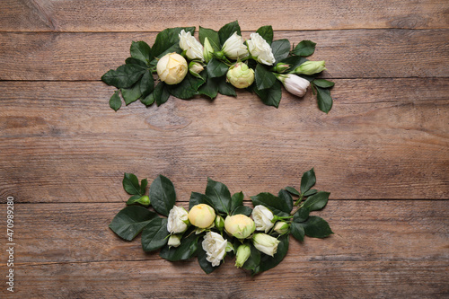 Wreath made of beautiful flowers and green leaves on wooden background, flat lay. Space for text