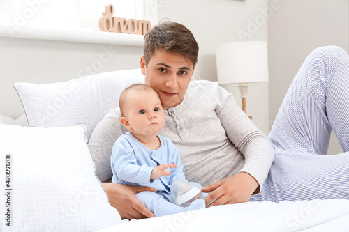 Young father with little baby boy and bottle of water in bedroom