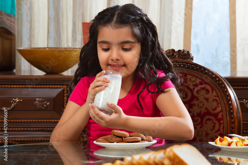 Little child girl drinking milk during breakfast at home photo