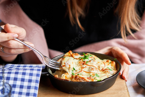 Potato with cheese casserole in a cast-iron frying pan. Close-up of a woman eating with a fork. Latvian cuisine