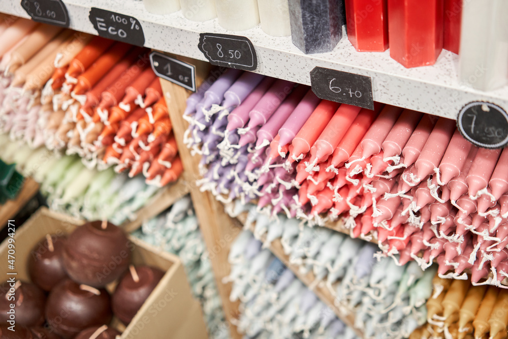 Many multicolored colorful paraffin stick Pastel colors candles arranged in shelves lying on shelter and sorted by color in a household candle shop store market.
