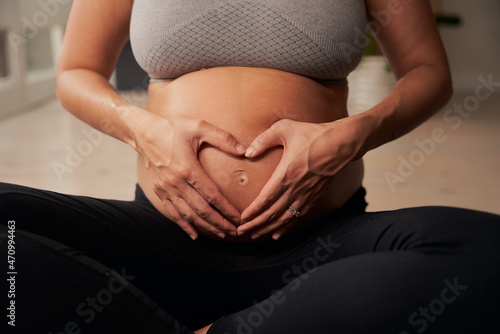 Caucasian pregnant mother sitting on yoga mat forming a heart shape with her hands on belly