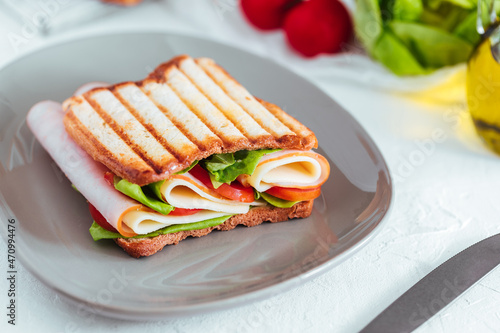 Toast sandwich with gouda cheese and turkey ham filled with tomato and lettuce on a bright background with ingredients in blurry background