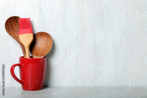 Set of wooden kitchen utensils in red cup on light grey table. Space for text