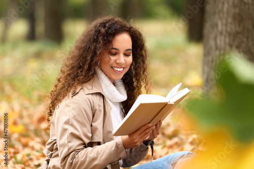 Happy African-American woman reading book in autumn park