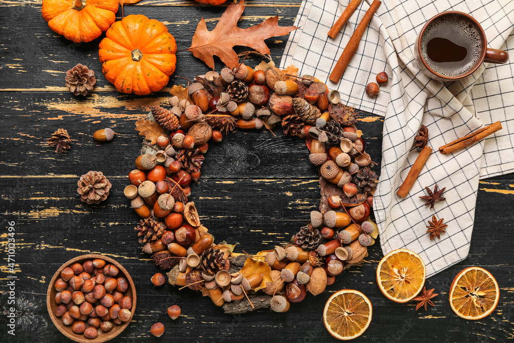 Beautiful acorn wreath, cup of coffee, pumpkins and hazelnuts on black wooden background - obrazy, fototapety, plakaty 