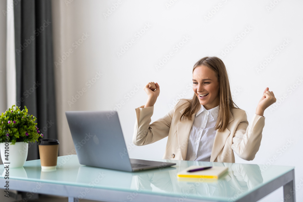 Excited smiling businesswoman celebrating business success at workplace, raising hands looking at laptop screen, feeling happy about great win Excited smiling businesswoman celebrating business success at workplace, raising hands looking at laptop screen, feeling happy about great win