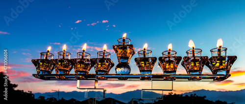 Crystal festive menorah and burning candles with olive oil as symbol of Hanukkah - Jewish Holiday of Miracle Light. Blurred background of mountains and dramatic sky cloud at sunset 