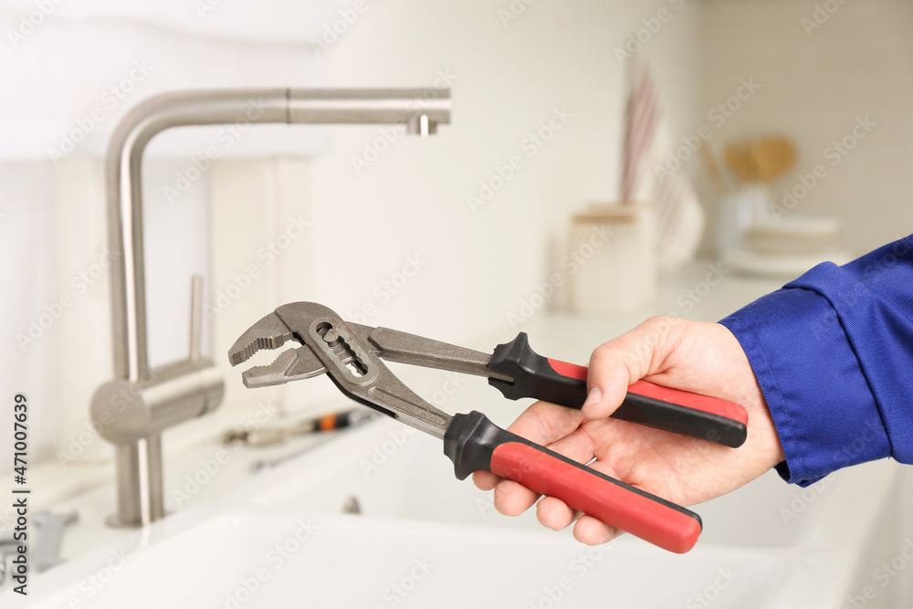 Plumber with spanner near sink in kitchen, closeup. Water tap installation Plumber with spanner near sink in kitchen, closeup. Water tap installation