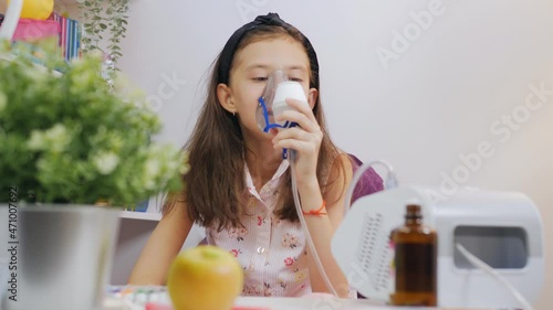 Little girl makes inhalation with medical nebulizer while sitting at the table.