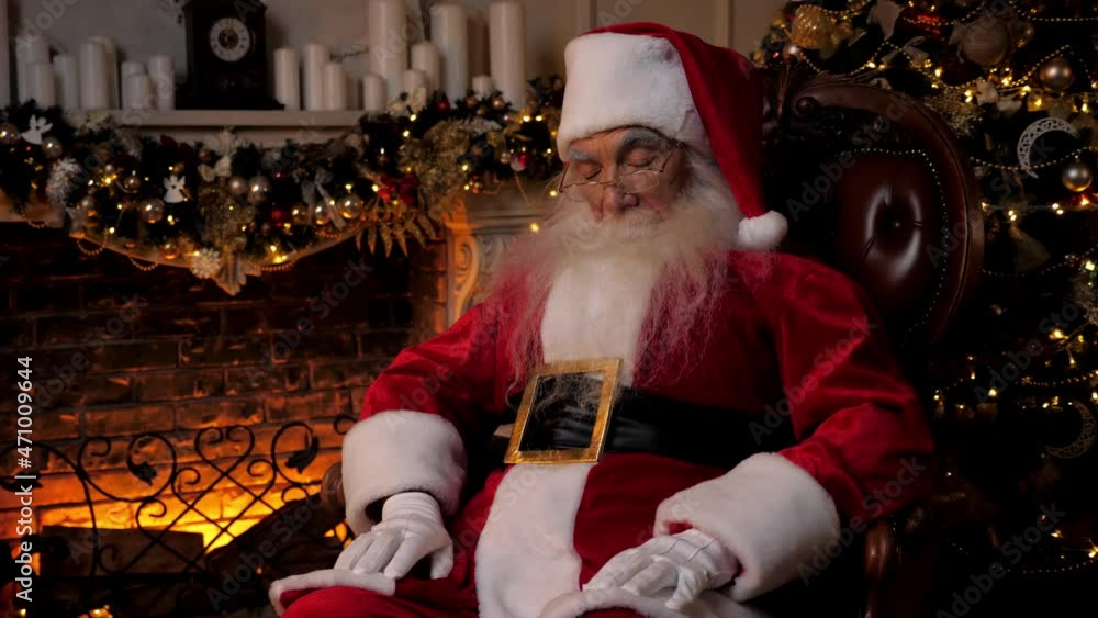 Santa Claus falls asleep while sitting on chair on background fireplace Christmas tree. Old man grandfather dressed as Santa Claus costume sleeping. New Year Christmas winter holidays celebration Santa Claus falls asleep while sitting on chair on background fireplace Christmas tree. Old man grandfather dressed as Santa Claus costume sleeping. New Year Christmas winter holidays celebration