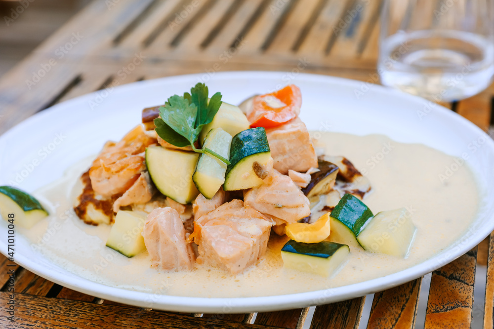 Salmon and vegetable dish with cream sauce on a plate, wooden table, outside Salmon and vegetable dish with cream sauce on a plate, wooden table, outside