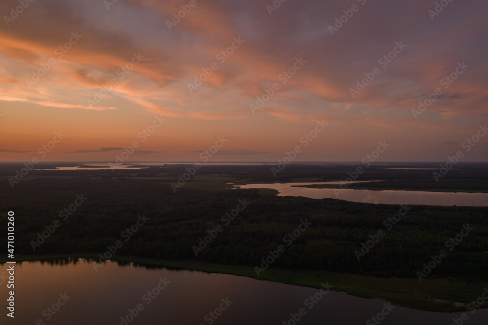 Aerial landscape of the lakes surrounded by the green forest. Blue sky and orange clouds during summer sunset.
