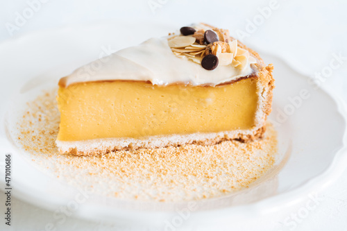 French flan on white plate with biscuit crumbs around, with almonds on top. Piece of cake on white bright background, traditional french  dessert photo