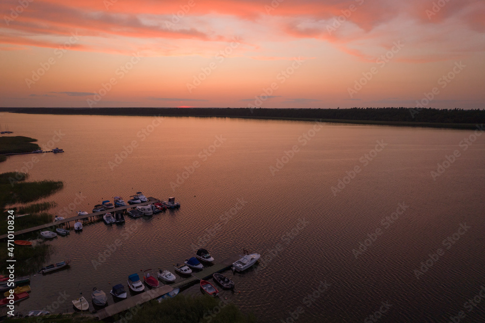 Fototapeta premium Sunset over the lake. Orange clouds during summer sunset. Motorboats docked at the marina.