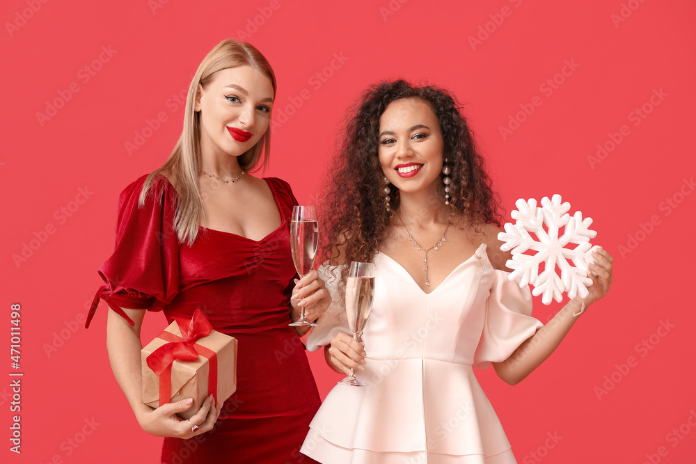 Beautiful young women with Christmas gift and glasses of champagne on color background Beautiful young women with Christmas gift and glasses of champagne on color background