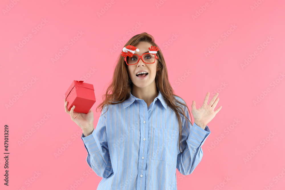 Attractive woman in Christmas glasses holds gift box on pink background Attractive woman in Christmas glasses holds gift box on pink background