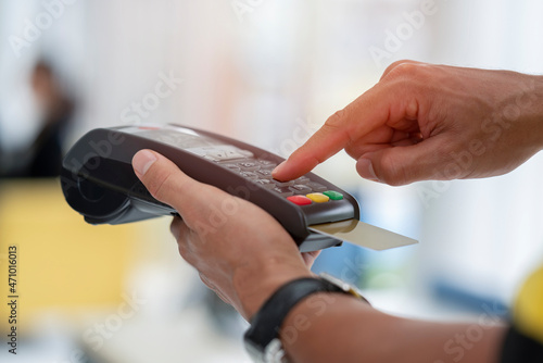 Cashier holding credit card reader machine on hand with insert card for payment process from customer  pressing the value number or price of products to charge the online payout  online deduction