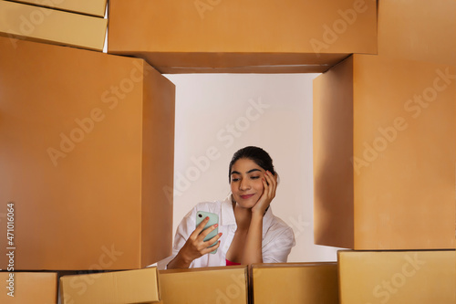 Adult girl watching Smartphone behind stacking of cardboard boxes photo