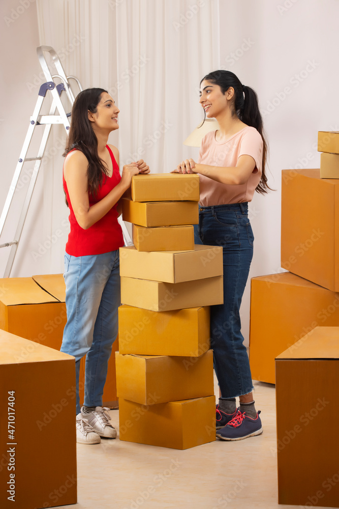 Adult girls standing together beside the stack of cardboard boxes Adult girls standing together beside the stack of cardboard boxes