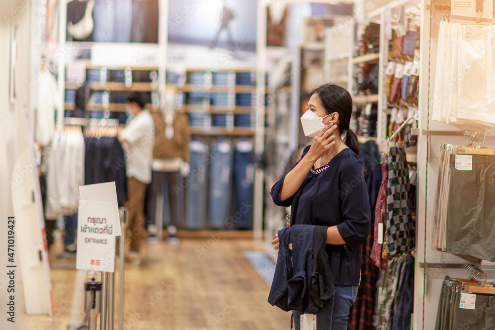 Adult woman in medical mask in a store. Buying clothing at the supermarket. Visiting public places during the coronavirus pandemic Adult woman in medical mask in a store. Buying clothing at the supermarket. Visiting public places during the coronavirus pandemic