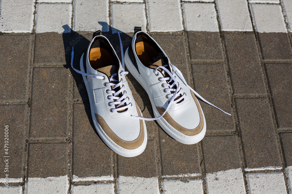 Men's feet in white everyday sneakers made of natural leather on lacing. Men's feet in white everyday sneakers made of natural leather on lacing.