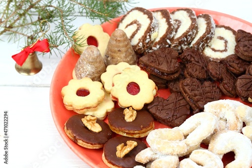 Christmas candies on the red plate and a bell. Typical traditional Xmas confectionery on the white wooden board, Europe.