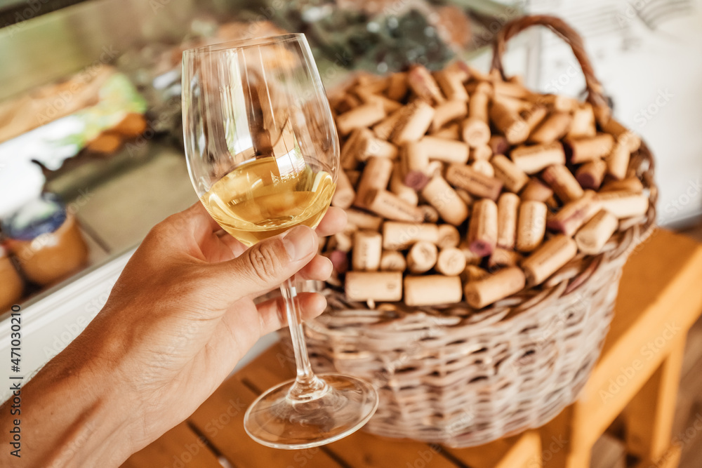 A glass of elite white wine on the background of a basket with a lot of corks at the winery.