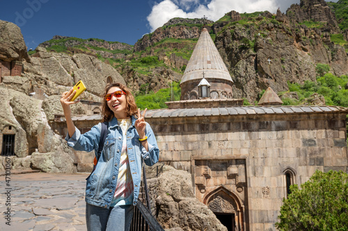 Woman tourist taking selfie photo at the background of Armenian Geghard Monastery. Travel blogger concept