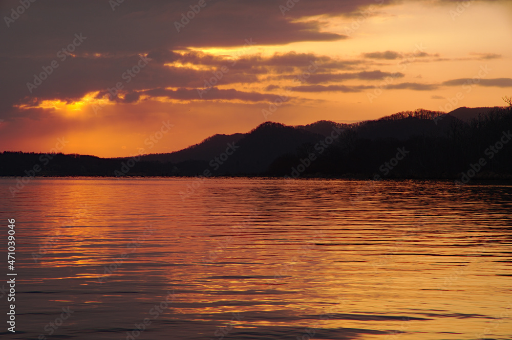 夜明けの光に黄金色に染まる湖。さざ波立つ湖面。