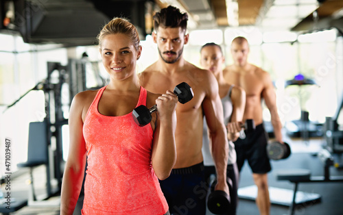 Group of athletic young people in sportswear with dumbbells exercising at the gym