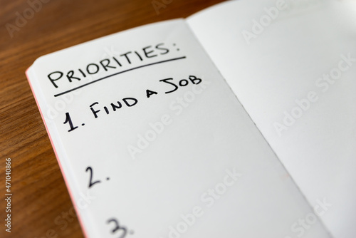 Blank page of notebook with text "priorities ... find a job", on wooden surface. Commitment to job search. 