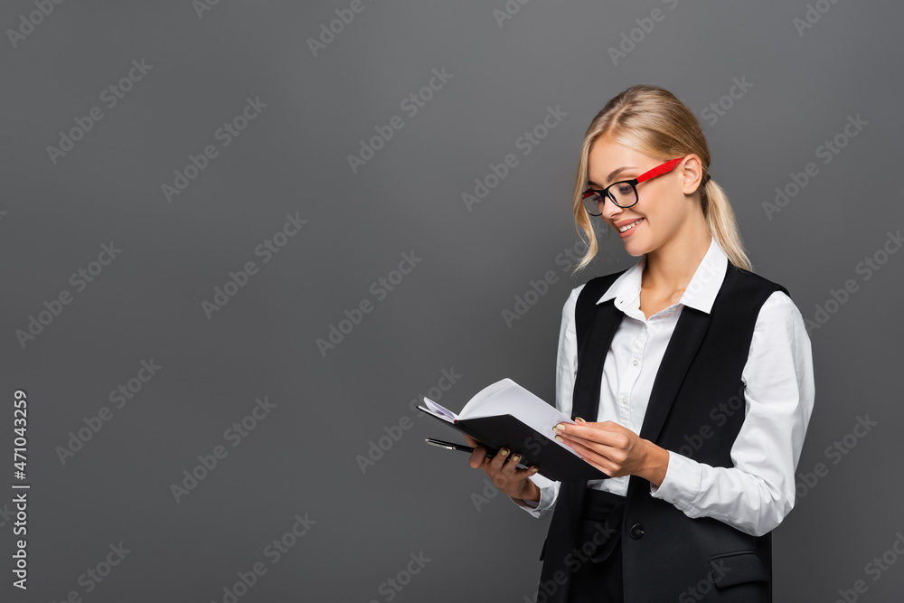 Smiling businesswoman holding pen and notebook isolated on grey Smiling businesswoman holding pen and notebook isolated on grey