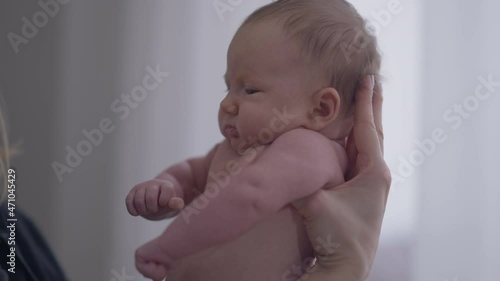 Side view little infant in female Caucasian hands indoors at home. Medium shot portrait naked baby girl with mother. Motherhood and infancy concept